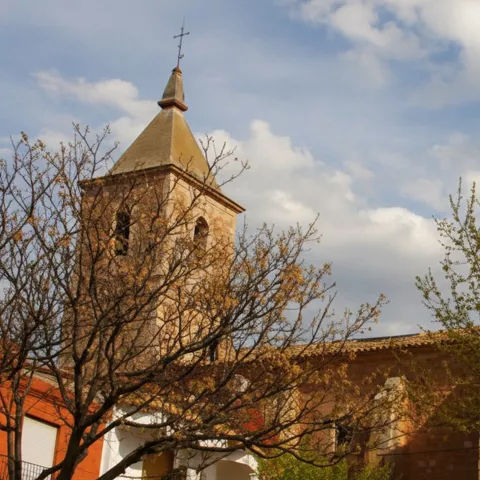 Iglesia de Motilleja rodeada de árboles y viviendas tradicionales en una plaza tranquila.