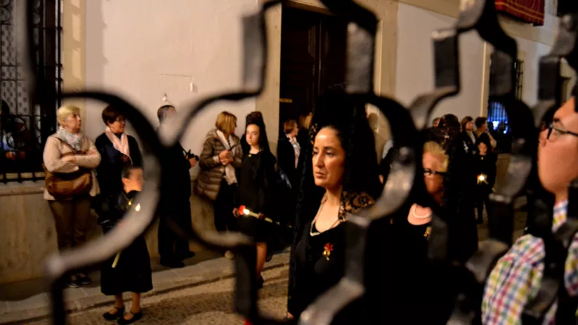 Participantes en procesión sosteniendo velas junto a la entrada de un templo
