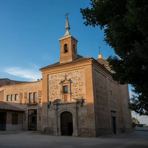 Pequeña iglesia de piedra y ladrillo con campanario y plaza despejada.
