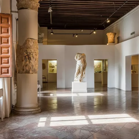 Sala con columnas de piedra, estatua y luz natural.
