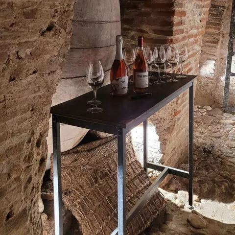 Mesa con botellas y copas dispuestas junto a una tinaja en bodega subterránea.