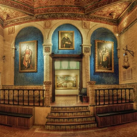 Sala histórica con arcos, techos decorados y cuadros religiosos enmarcados.