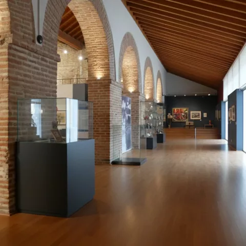 Galería amplia con arcos de ladrillo, suelo de madera y obras en las paredes.