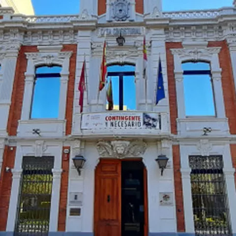 Detalle frontal de un edificio institucional con balcones, escudos decorativos y puertas de madera.