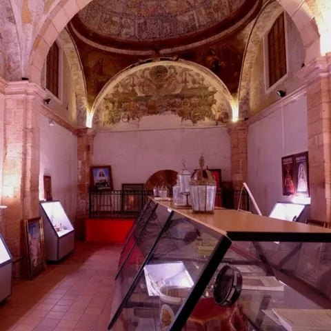 Interior de museo con frescos en el techo y vitrinas de vidrio en primer plano.