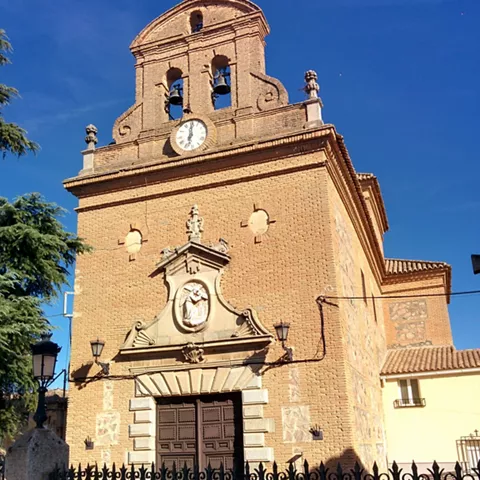 Fachada de iglesia de ladrillo con espadaña, campanas y reloj