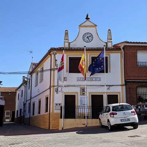 Fachada de ayuntamiento con reloj, banderas y coche blanco