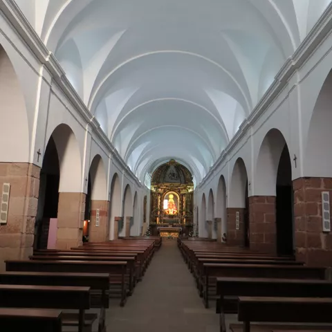 Nave central con bóvedas blancas y bancos alineados hacia el altar.
