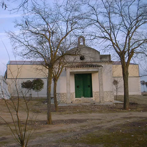 Pequeña ermita blanca con puerta verde entre árboles