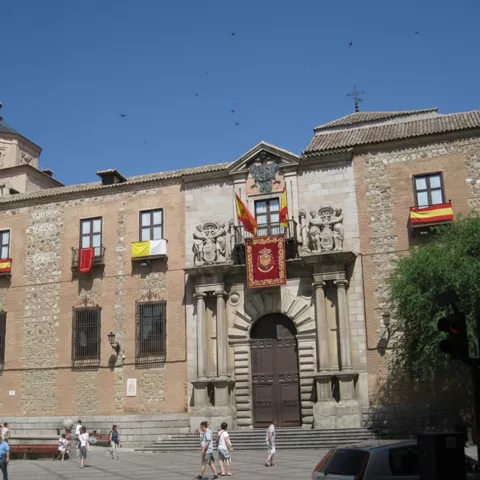 Fachada con banderas y escudos sobre puerta principal de piedra.