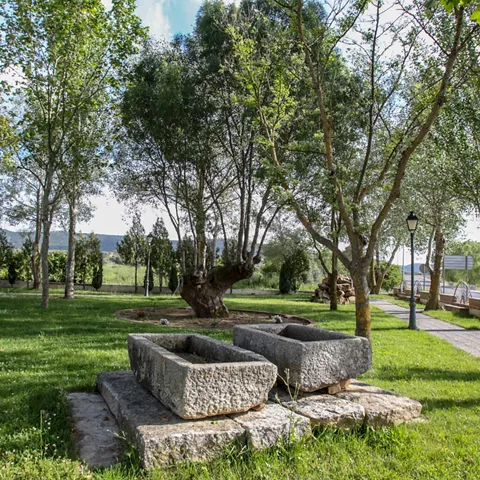 Zona ajardinada con árboles, antiguas pilas de piedra y senderos peatonales.