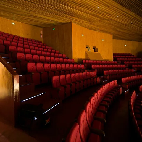 Interior de sala con filas de butacas rojas y salida iluminada al fondo.