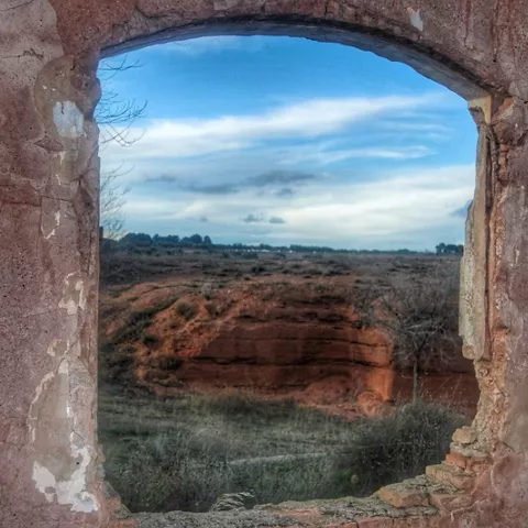 Ventana en ruinas con paisaje árido al fondo.