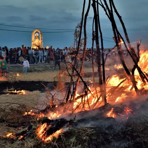 Personas y niños cerca de una gran hoguera al atardecer.