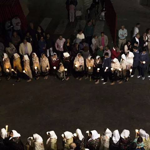 Vista aérea de participantes formando un círculo con velas en una plaza de noche.