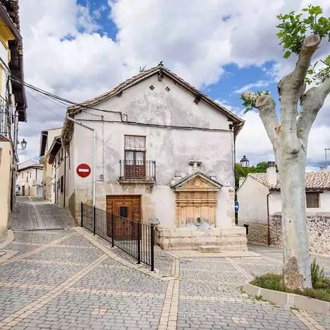 Calle empedrada con casas tradicionales y una fuente mural.