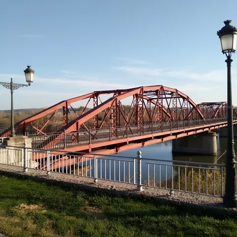 Puente metálico rojo visto desde un paseo con farolas y barandilla.