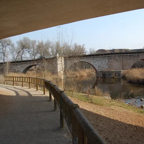 Sendero fluvial junto a puente histórico.