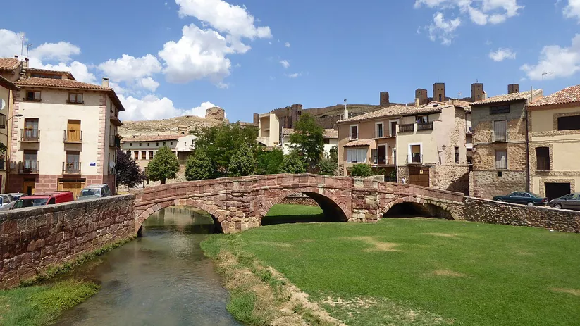 Puente de piedra sobre río con murallas al fondo.