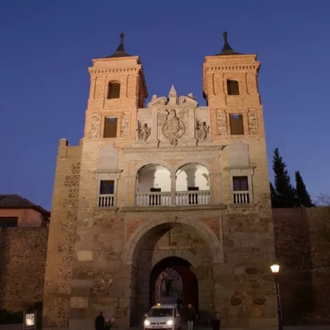 Entrada iluminada al anochecer con arco y vehículo atravesando.