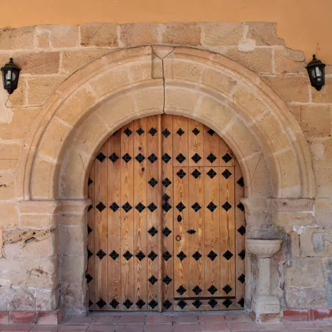 Puerta de madera con herrajes bajo arco de piedra.