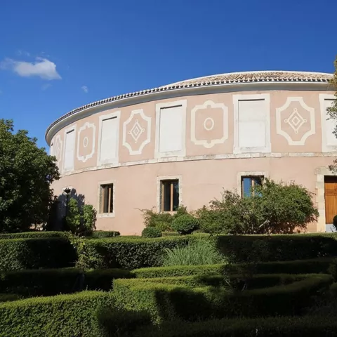 Edificio circular de fachada rosada con jardines geométricos en primer plano.