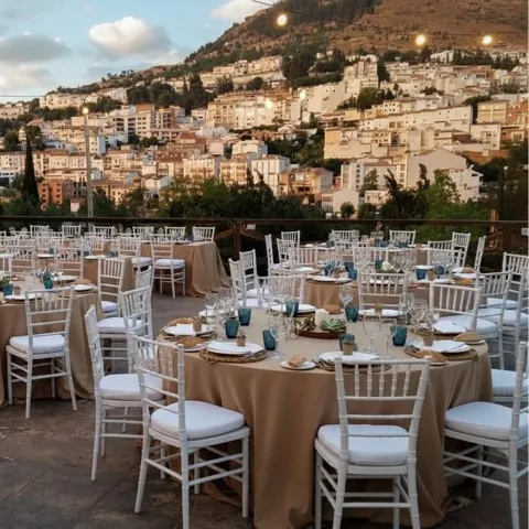 Terraza con mesas preparadas para evento, con vistas a una ciudad en ladera al atardecer.