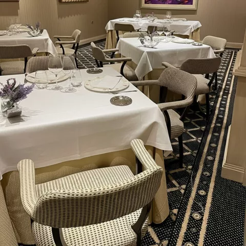 Comedor elegante con mesas vestidas, sillones tapizados y cuadros en las paredes.