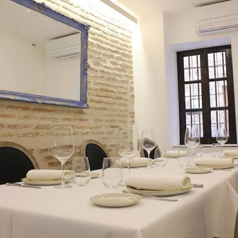 Mesa alargada con mantel blanco junto a pared de ladrillo visto y espejo decorativo.