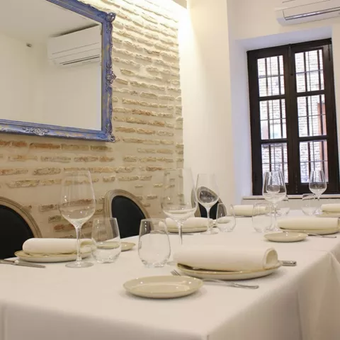 Comedor íntimo con mesa vestida en blanco, pared de ladrillo visto y espejo decorativo.