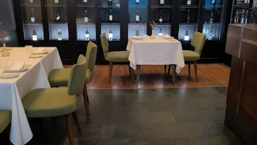 Sala de restaurante con vitrina iluminada de botellas y mesas vestidas.