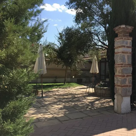 Terraza ajardinada con suelo de piedra, sombrillas y columnas.