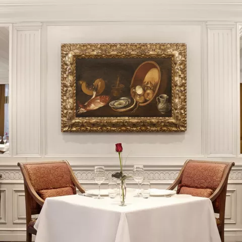 Mesa para dos bajo cuadro barroco en comedor de estilo tradicional con molduras blancas.