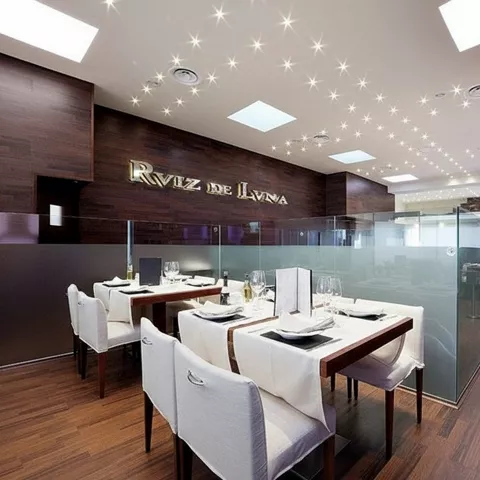 Interior de restaurante con escalera, vitrinas iluminadas y divisiones de cristal esmerilado.