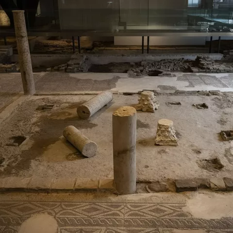 Restos arqueológicos con mosaicos y columnas bajo estructura de cristal.