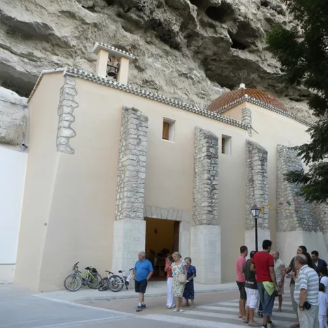 Ermita adosada a un acantilado, con gente reunida en la plaza de entrada.