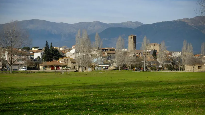 Vista de un pueblo con campo verde y montañas al fondo