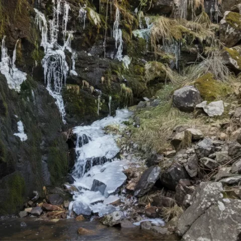 Cascada estrecha cayendo por una garganta rocosa hacia una poza con piedras.