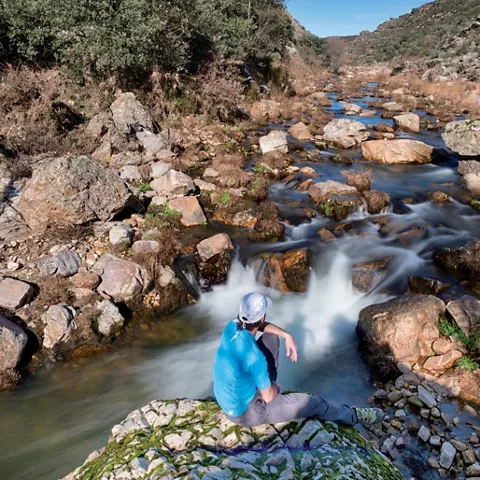 Hombre junto a pequeña cascada en arroyo.