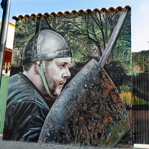 Mural de guerrero con casco y escudo en un entorno boscoso.