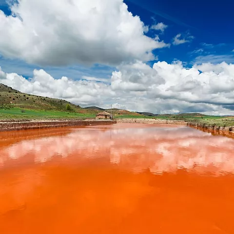 Agua salina anaranjada con reflejos del cielo