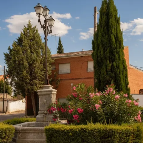 Farola de plaza rodeada de cipreses y flores