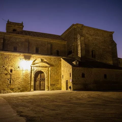 Una vista nocturna de una gran iglesia de piedra iluminada por luces cálidas, con un cielo azul oscuro.