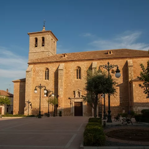 Iglesia de piedra en una plaza, con torre y farolas frente a la entrada.