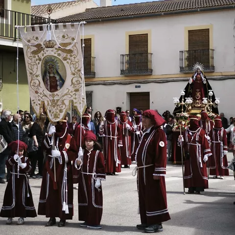 Nazarenos con túnicas granates portando estandarte durante una procesión diurna.