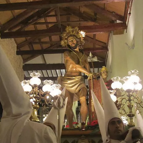 Paso procesional con figura religiosa iluminada por candelabros en el interior de un templo.