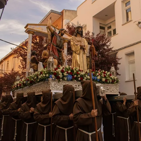 Procesión al atardecer con cofrades y paso con figuras religiosas.