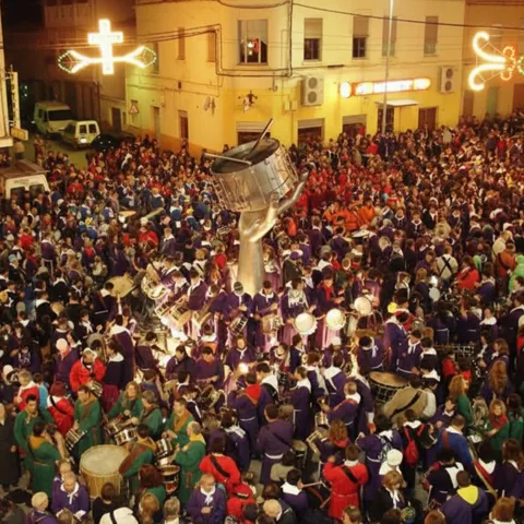 Multitud nocturna rodea escultura mientras cofradías tocan tambores en la plaza.