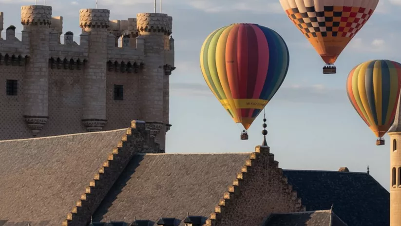 Varios globos aerostáticos de colores sobrevolando torres y tejados históricos.