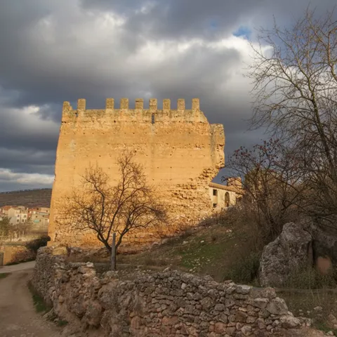 Torre defensiva del castillo de Socovos junto a un camino de piedra y árboles.